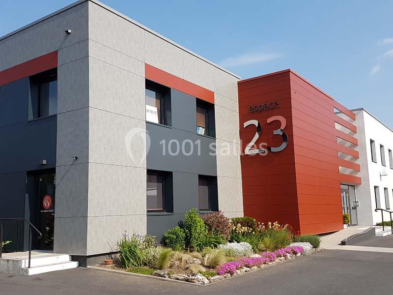 Bâtiment moderne avec façade grise et rouge, marqué ’espace 23’, entouré de végétation et d'un chemin pavé.