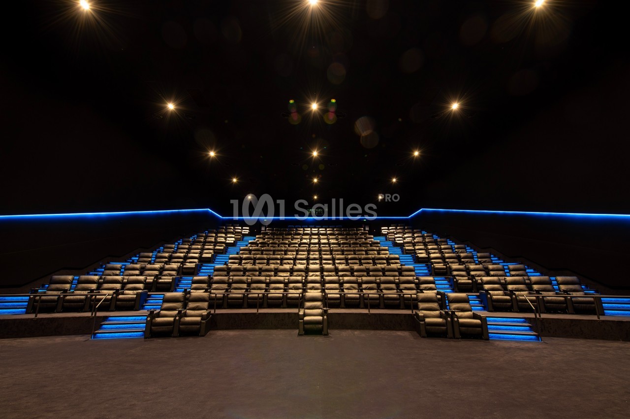 Salle de cinéma vide avec des rangées de sièges inclinables et des éclairages bleus sur les marches.