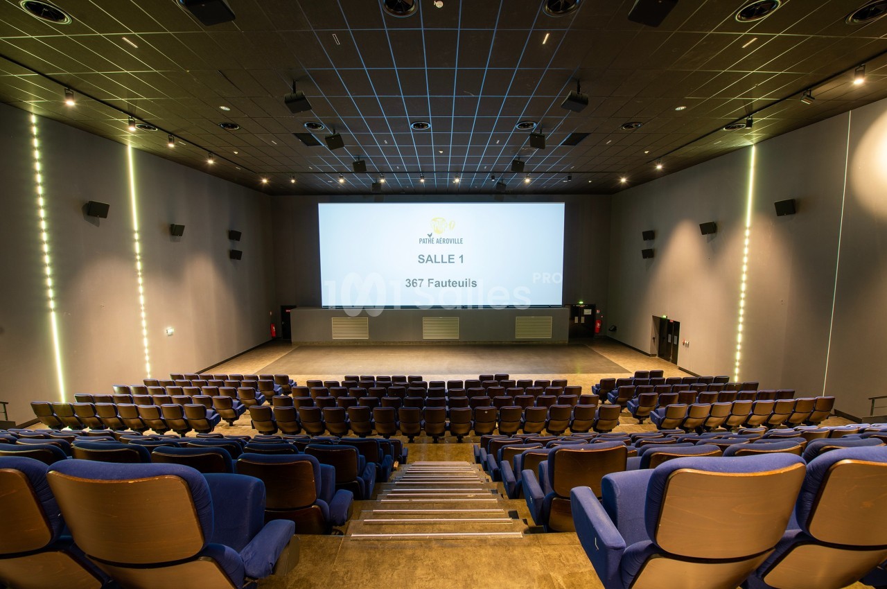 Salle de cinéma vide avec rangées de fauteuils bleus, écran géant allumé et éclairage tamisé.