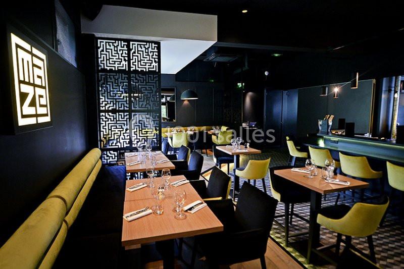 Salle de restaurant moderne avec tables en bois, chaises vertes et noires, éclairage tamisé et décorations murales…