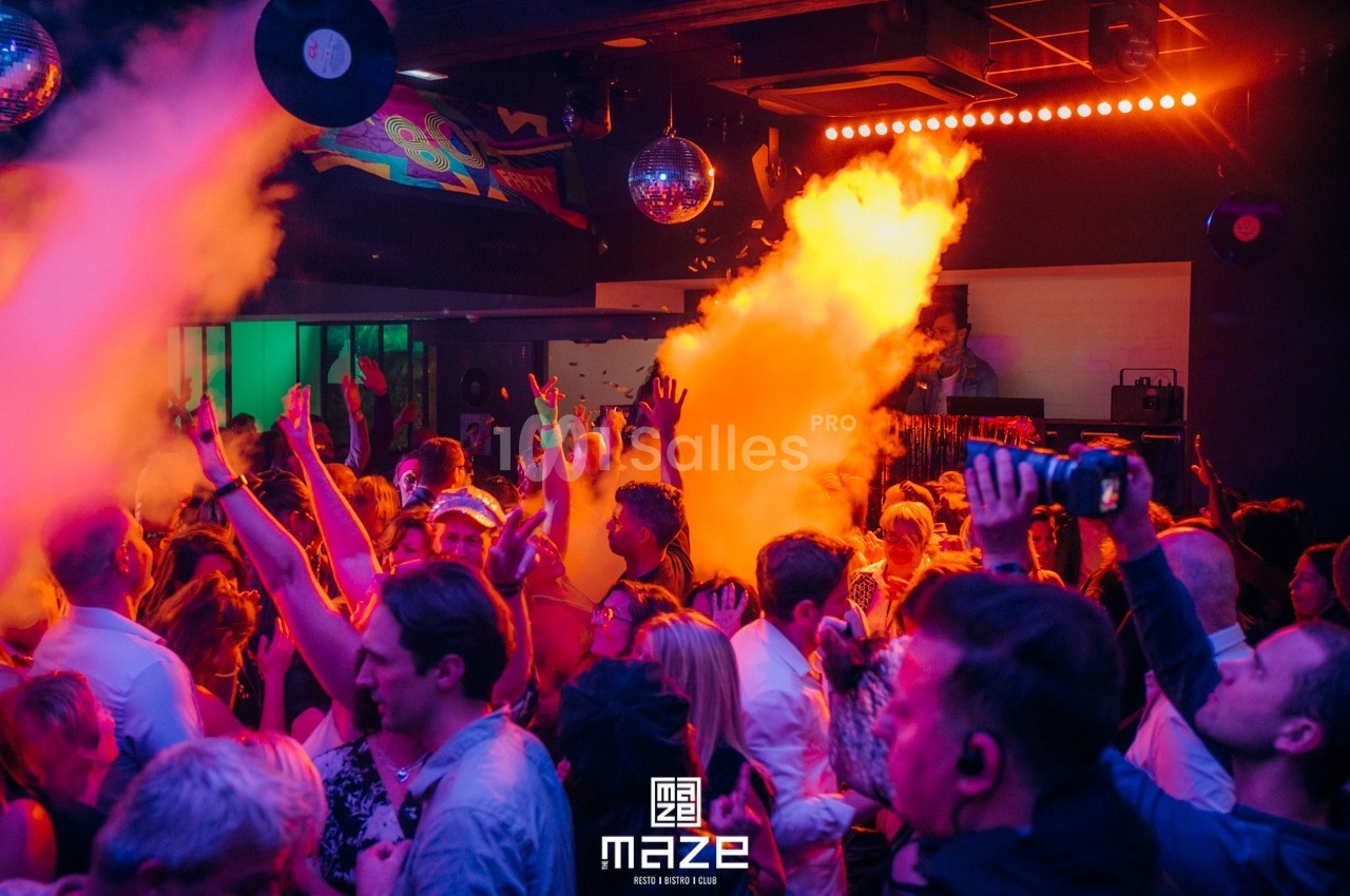 Foule dansante dans une discothèque avec jeux de lumière colorés et fumée orange.