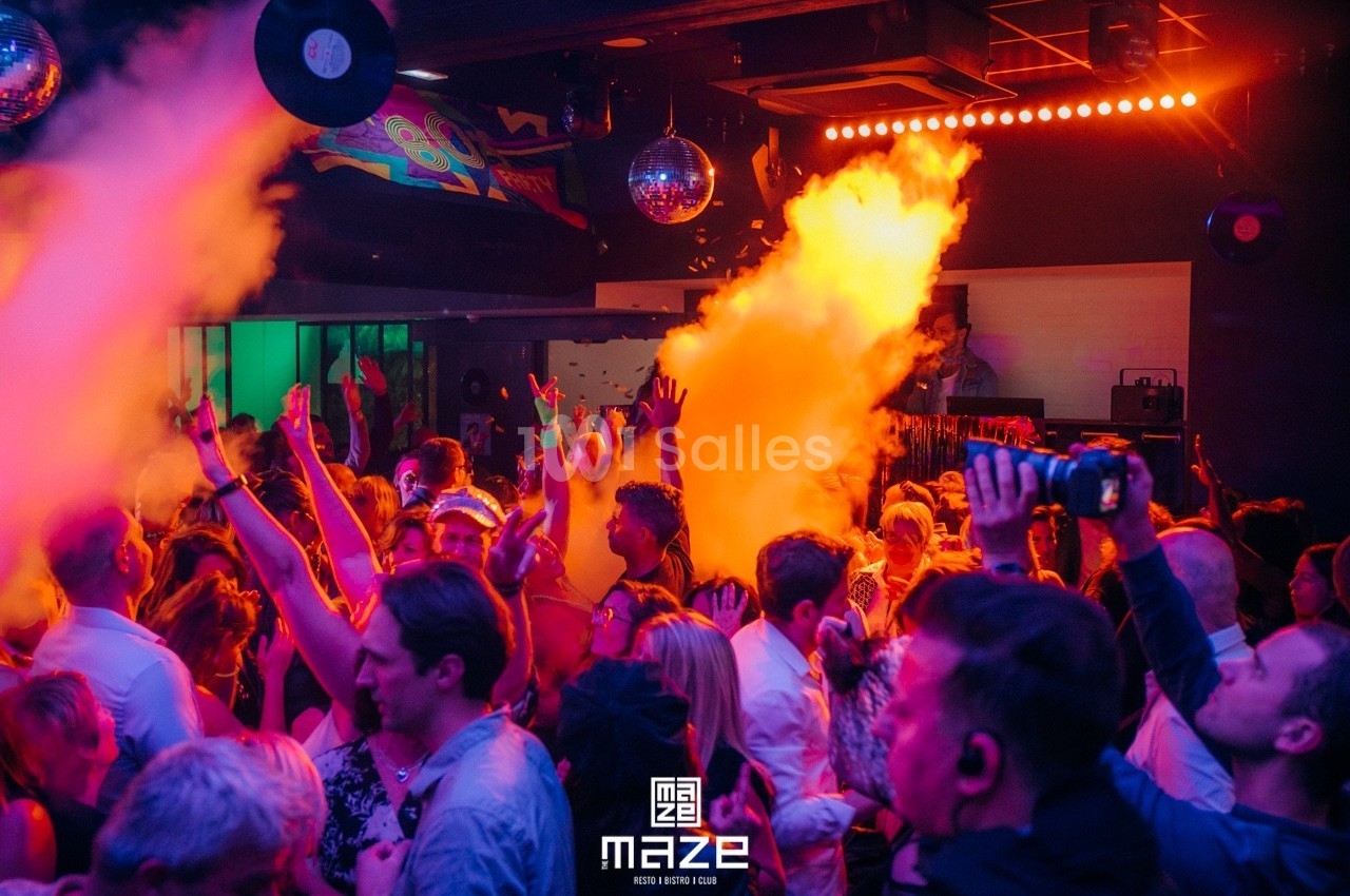 Foule dans une discothèque animée avec jeux de lumière colorés et fumée, ambiance festive et dansante.
