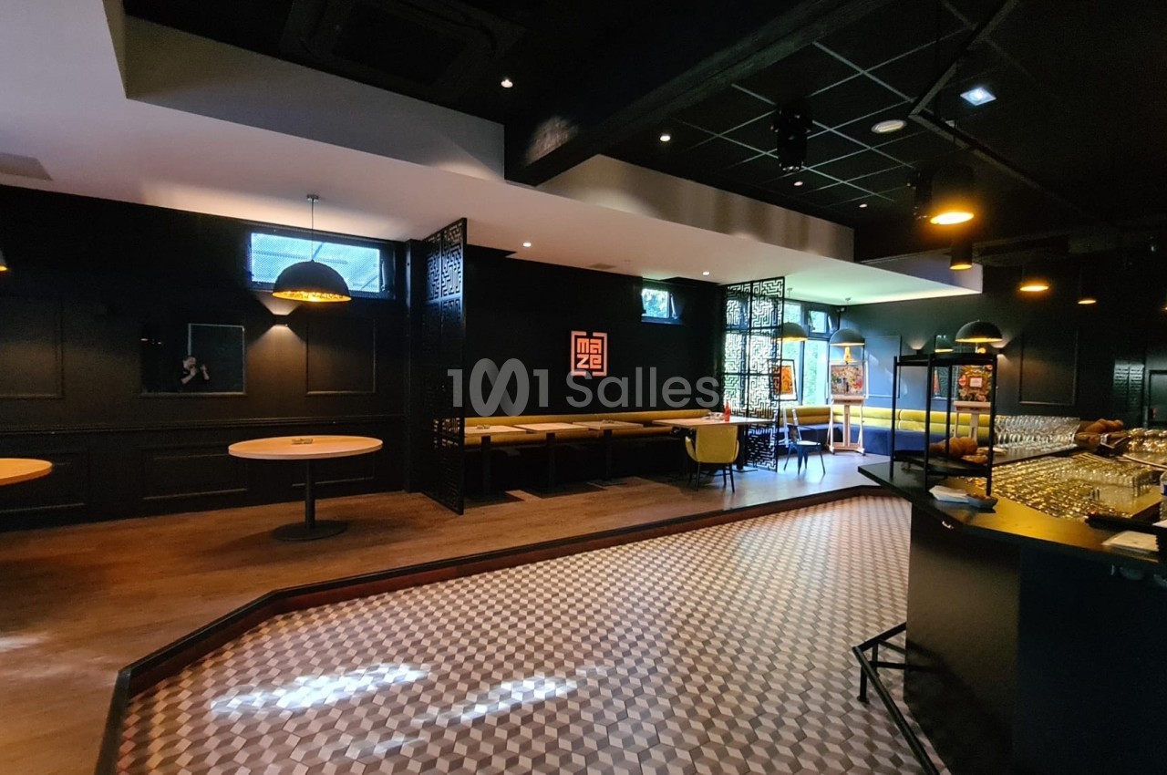 Salle de restaurant moderne avec tables, banquettes, bar et éclairage tamisé dans une ambiance sombre et élégante.