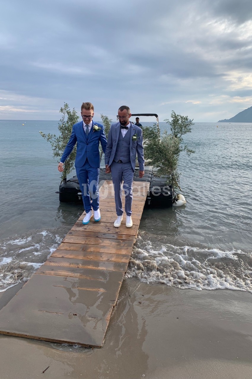 Deux hommes en costume marchant main dans la main sur un ponton en bois au bord de la mer.