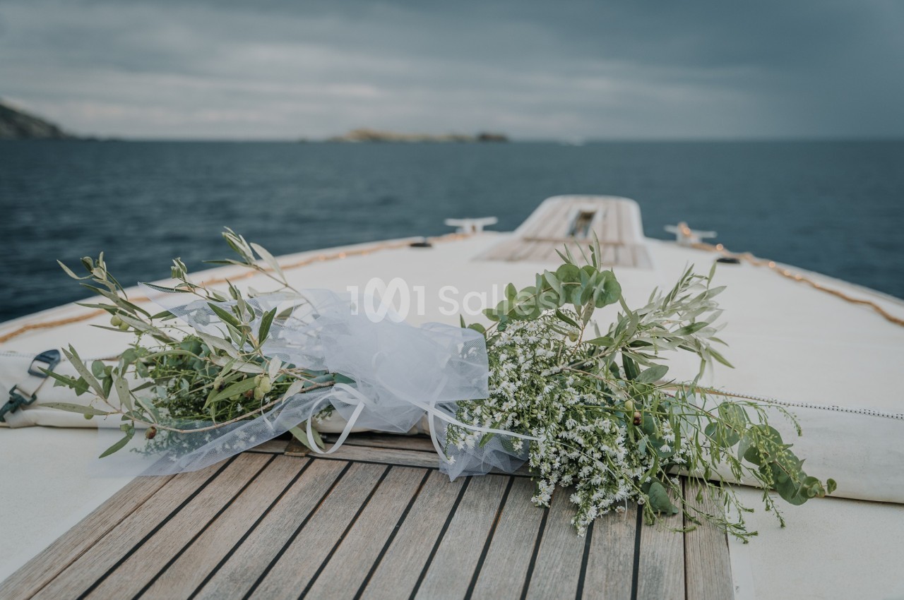 Bouquet de fleurs blanches et feuillages verts posé sur le pont en bois d'un bateau, avec la mer en arrière-plan.