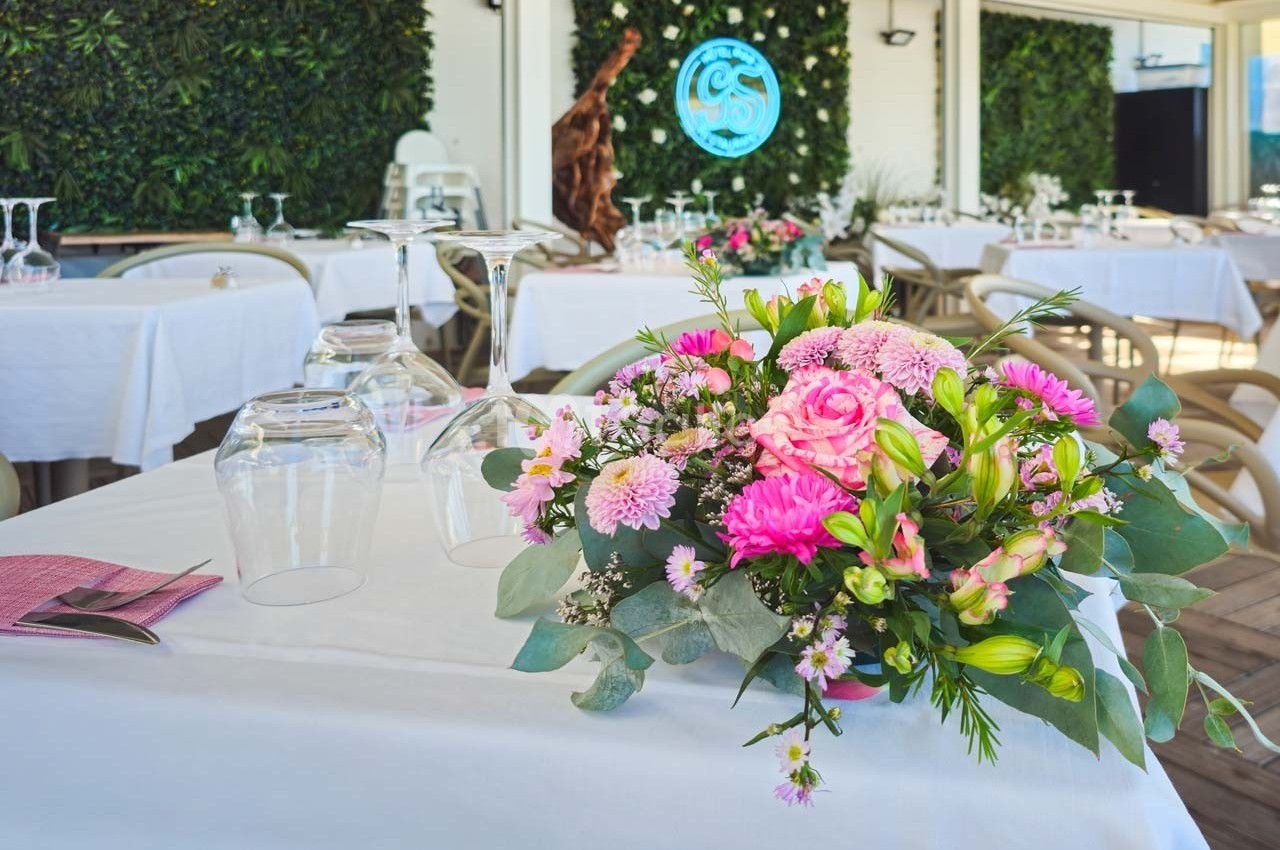 Bouquet de fleurs roses et blanches sur une table dressée dans un restaurant avec mur végétal en arrière-plan.
