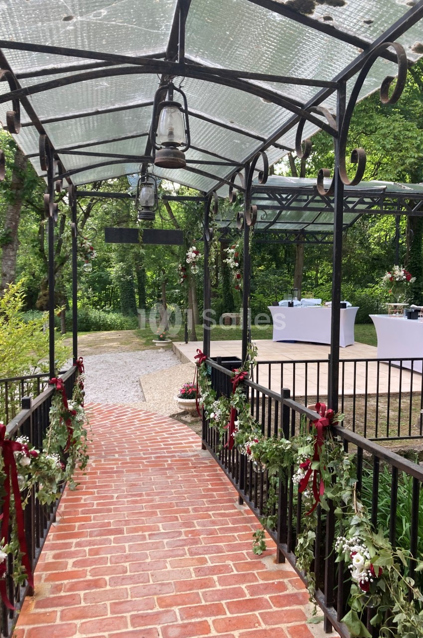 Passage en brique couvert de fer forgé décoré de fleurs, menant à une terrasse aménagée pour un événement en plein air.