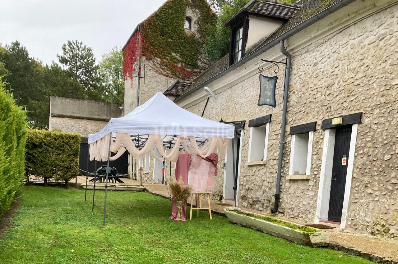 Tente blanche décorée installée sur une pelouse devant un bâtiment en pierre avec des volets noirs.