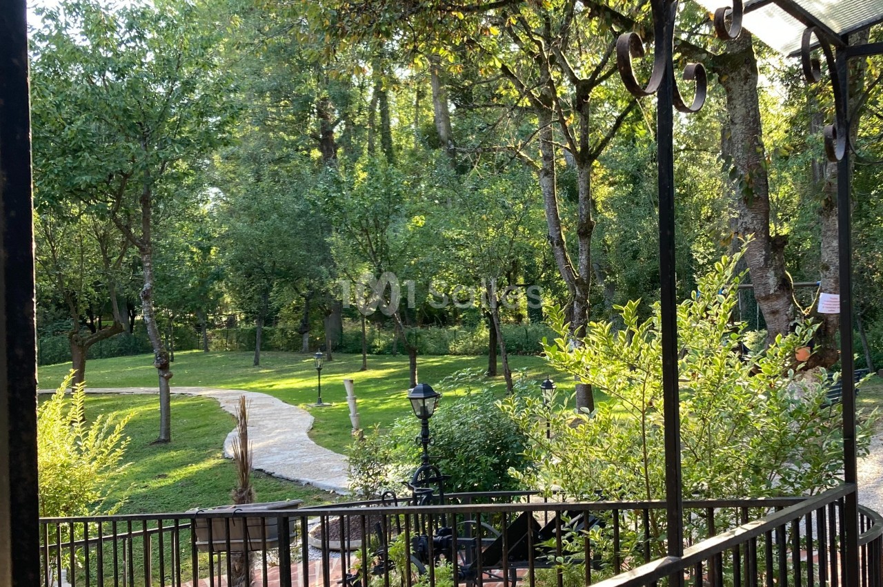 Vue sur un jardin verdoyant avec des arbres, un chemin sinueux et une balustrade en premier plan.