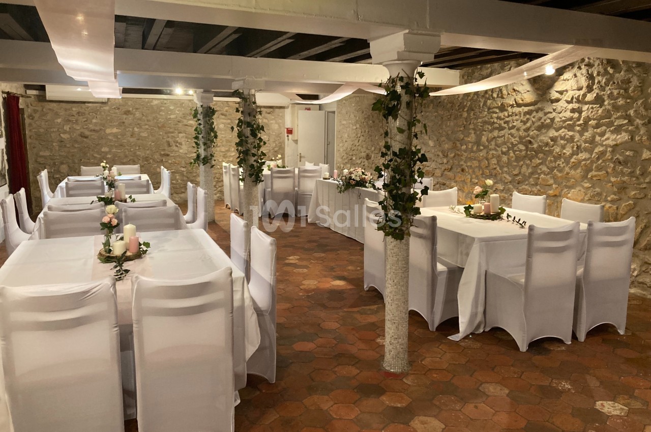 Salle de réception décorée avec des tables blanches, des chaises houssées et des guirlandes de feuillage sur les colonnes.