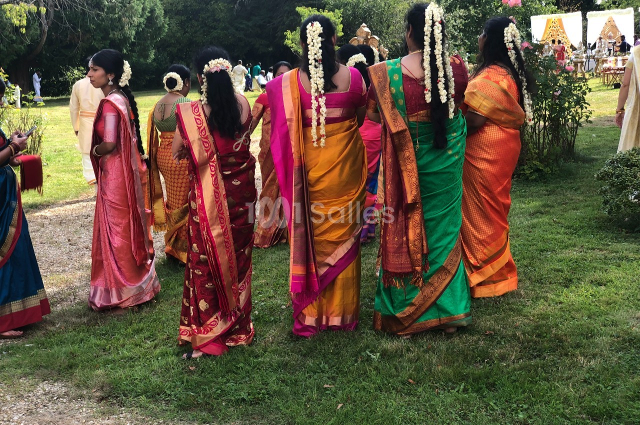 Des femmes en saris colorés avec des guirlandes de fleurs dans les cheveux, debout dans un jardin lors d'un événement.