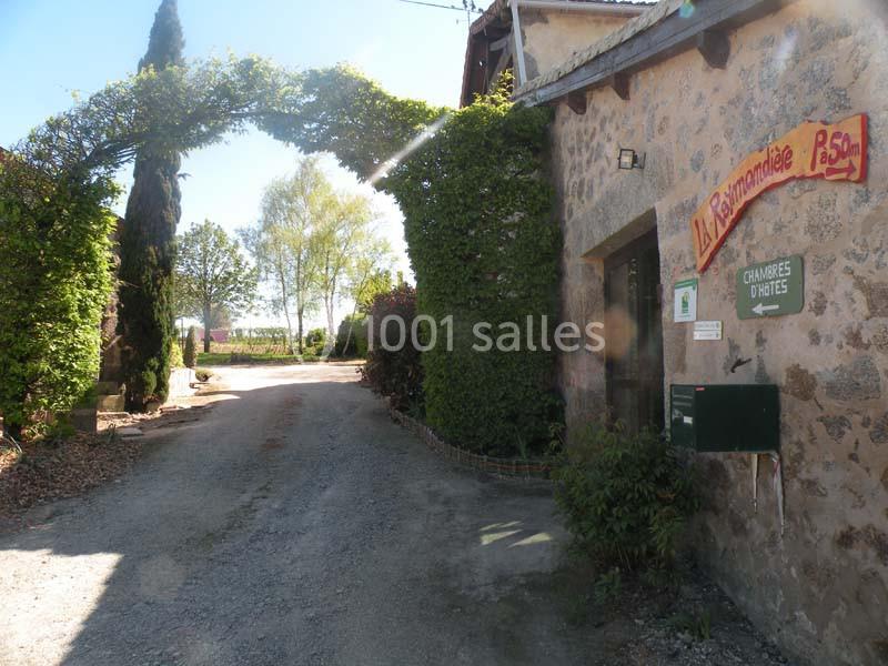 Entrée d'une maison en pierre avec un panneau indiquant des chambres d'hôtes, entourée de végétation et d'une arche végétale.
