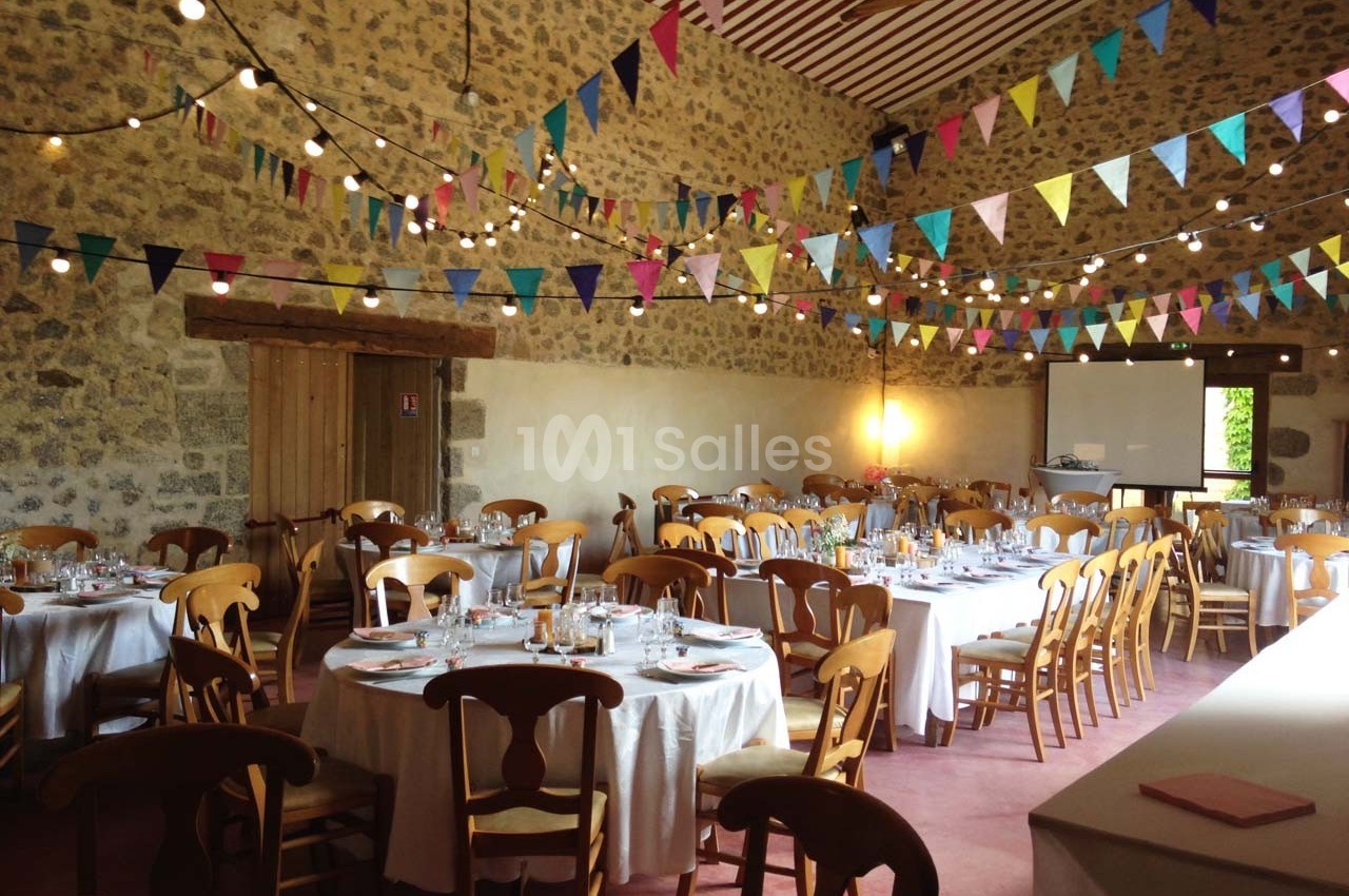 Salle de réception décorée avec des guirlandes colorées et des tables rondes dressées pour un événement.
