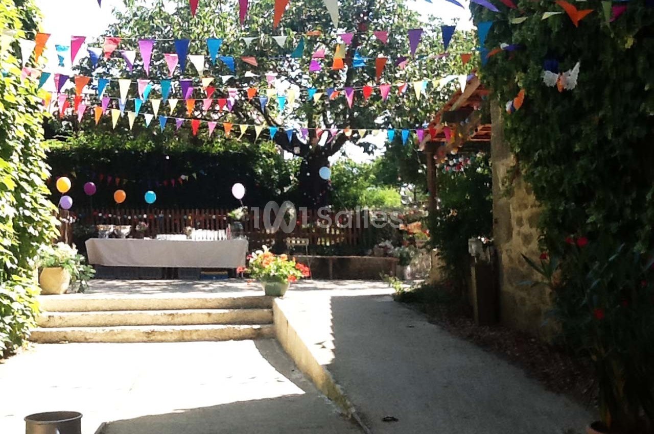 Cour extérieure décorée de guirlandes colorées et de ballons, avec une table dressée sous un arbre.