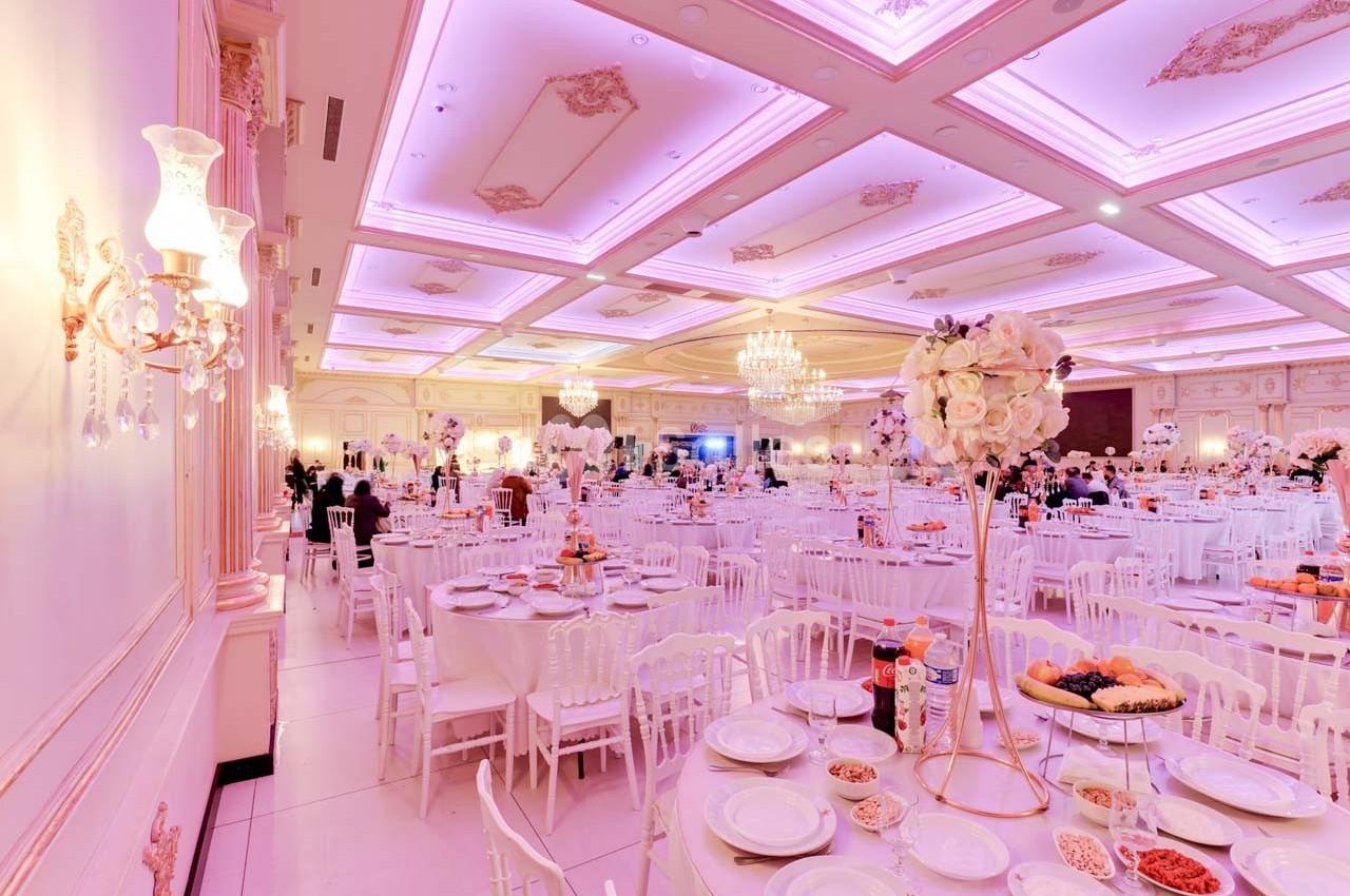 Salle de réception élégante décorée de tons roses et blancs, avec tables dressées et éclairage chaleureux.