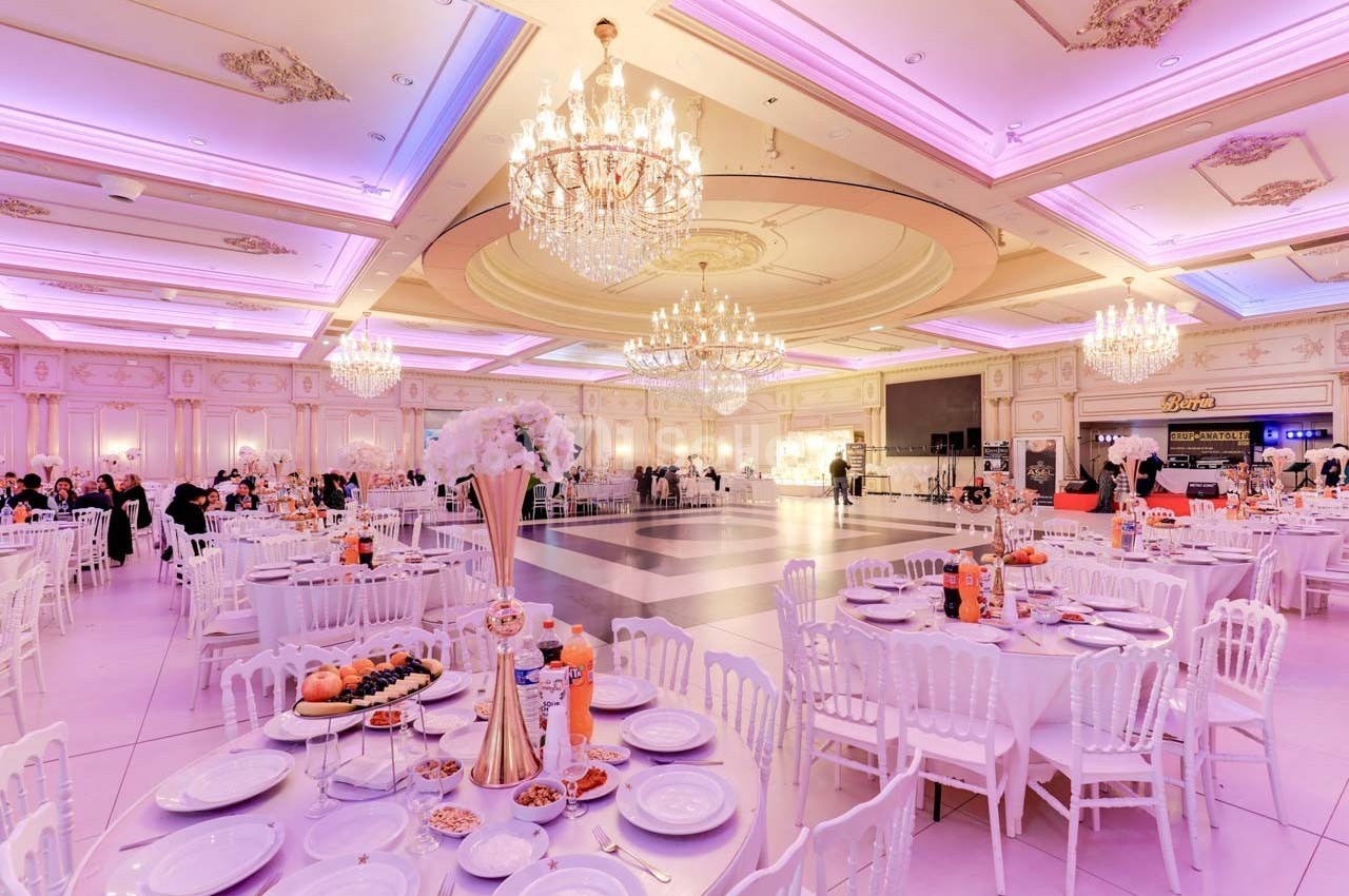 Salle de réception élégante avec tables dressées, chandeliers imposants et éclairage rose tamisé.