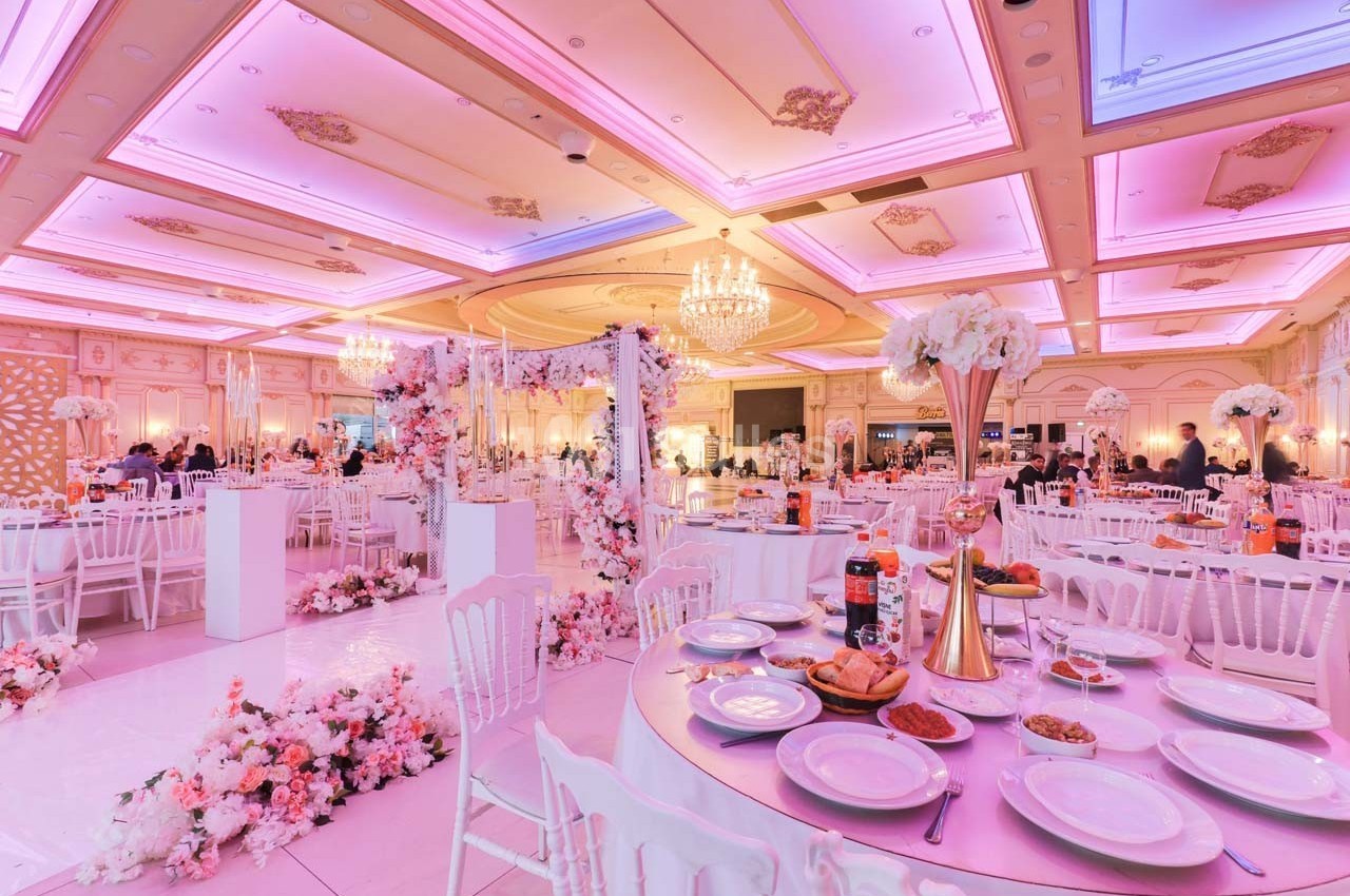 Salle de réception décorée avec des fleurs roses, tables dressées et éclairage rose chaleureux.