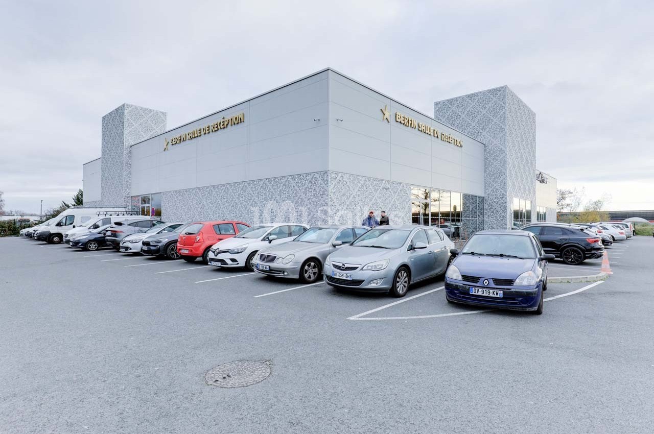 Parking avec plusieurs voitures devant un grand bâtiment moderne aux façades claires et décoratives.