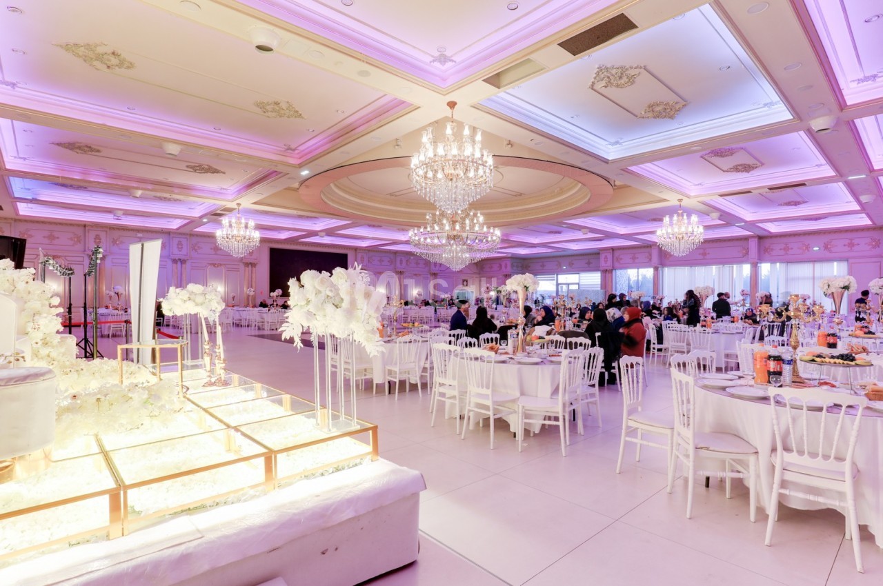 Salle de réception élégante avec tables décorées, lustres imposants et éclairage rose tamisé.