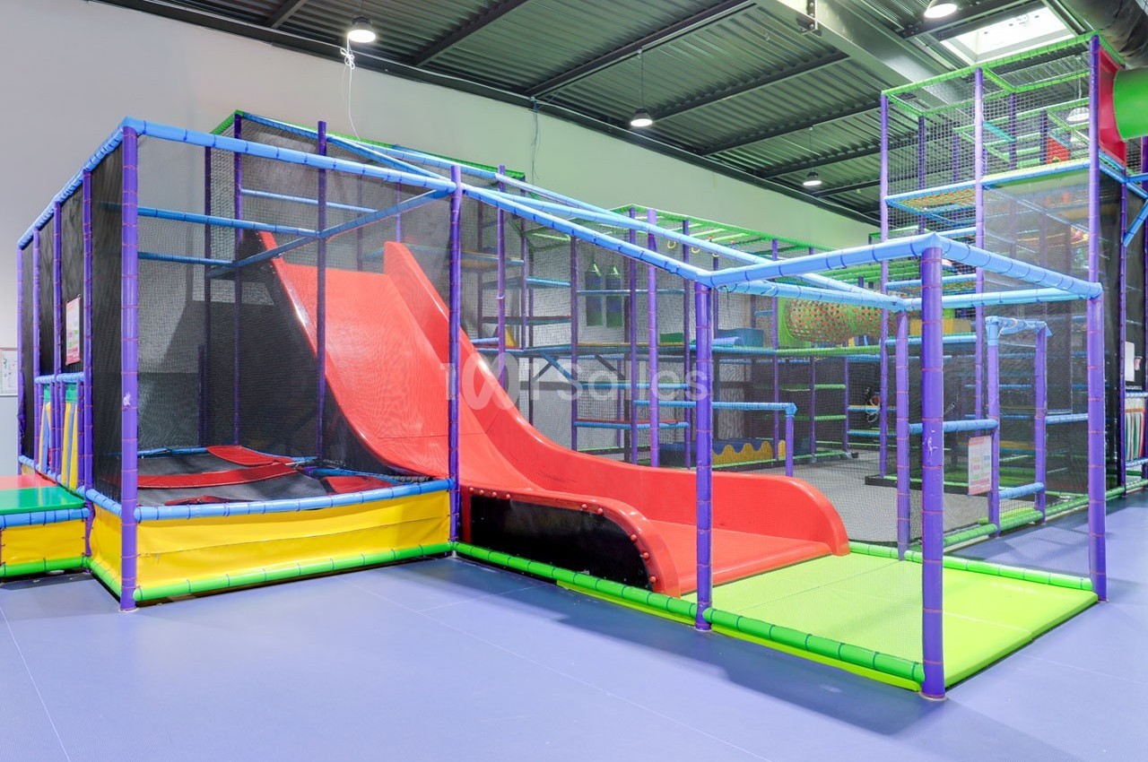 Structure de jeu intérieure avec toboggans rouges, tunnels et filets, conçue pour les enfants dans un espace couvert.
