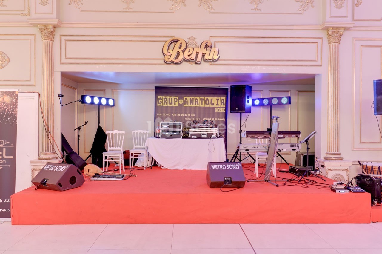 Scène intérieure avec équipements audio, éclairages, instruments et une bannière du groupe ’Grup Anatolia’.