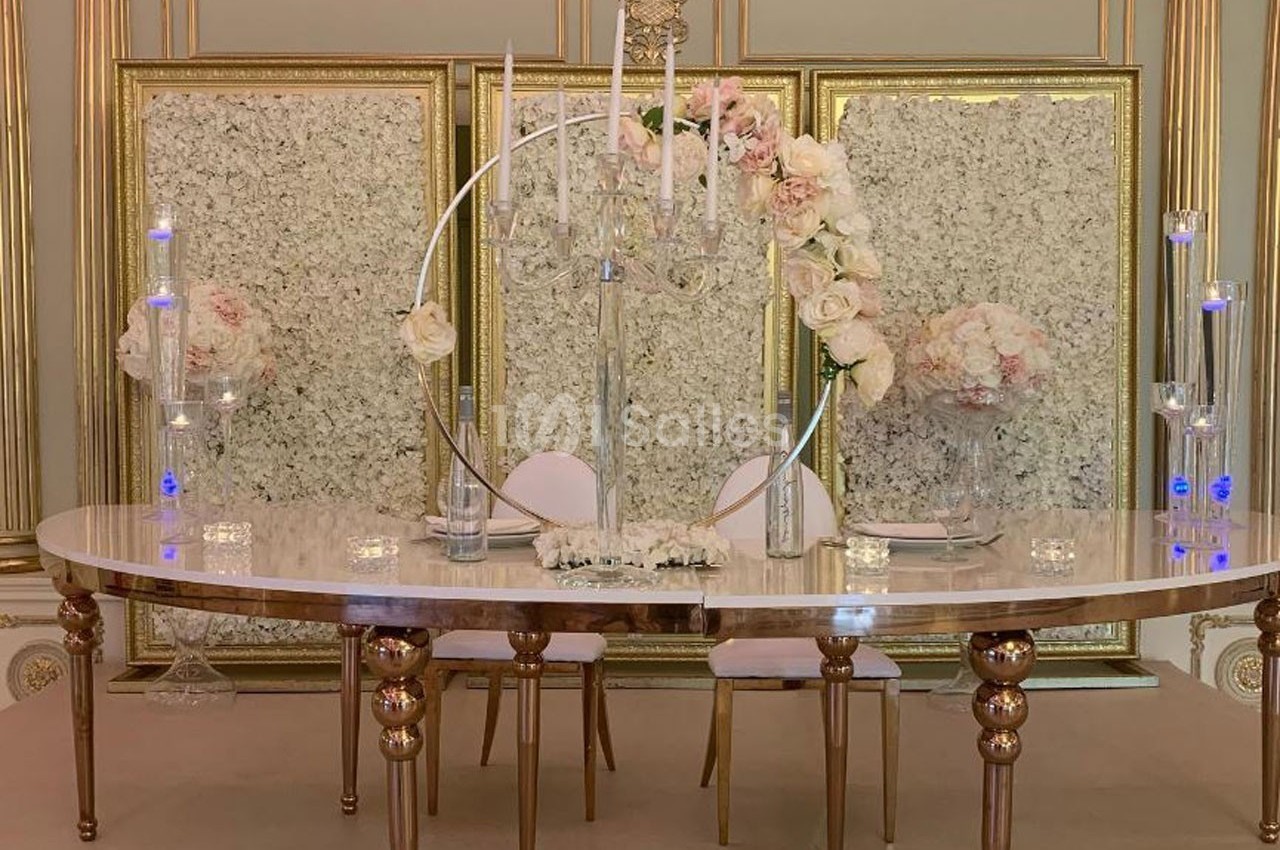 Table décorée avec des chandeliers, des fleurs blanches et roses, devant des panneaux ornés de motifs floraux.