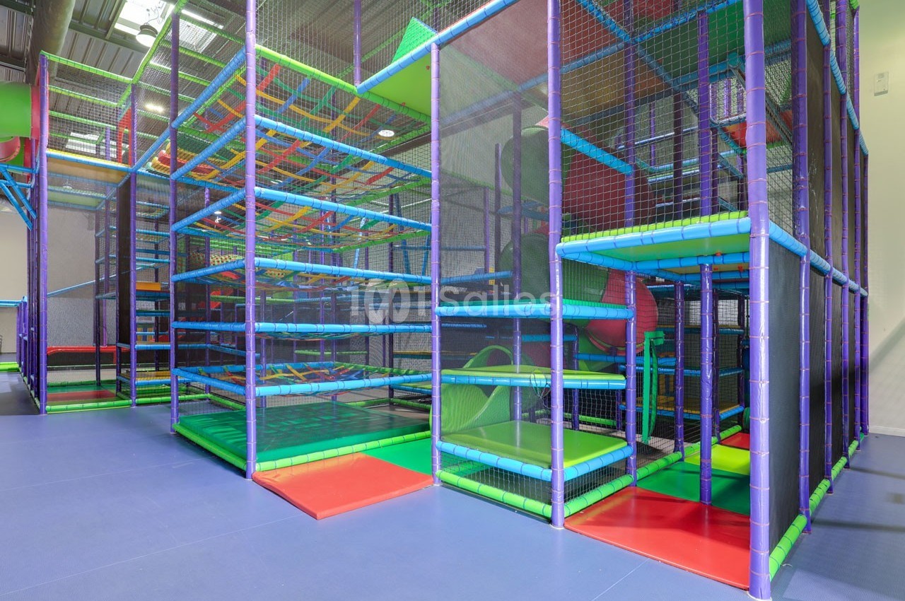 Structure de jeux pour enfants en intérieur avec toboggans, plateformes colorées et filets de sécurité.