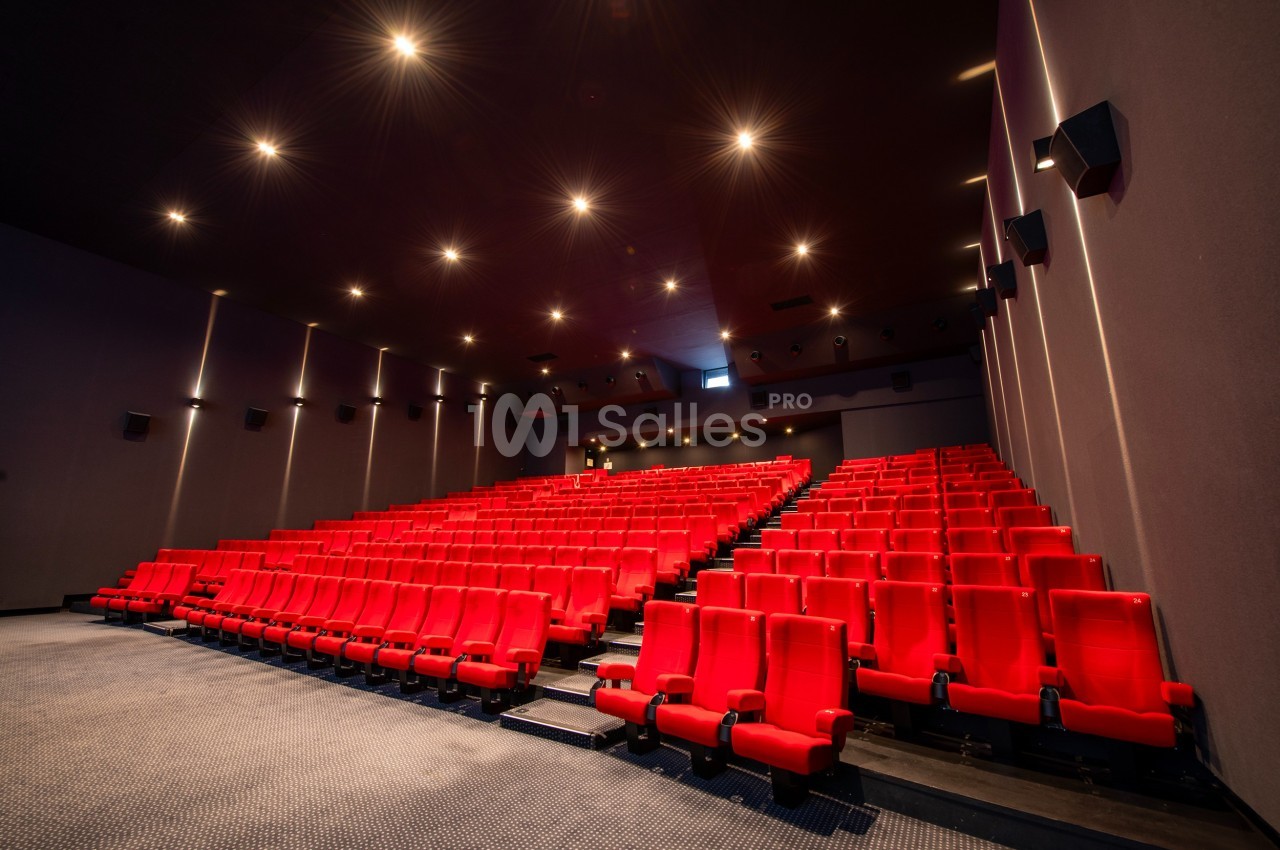Salle de cinéma vide avec des rangées de sièges rouges et un éclairage tamisé.