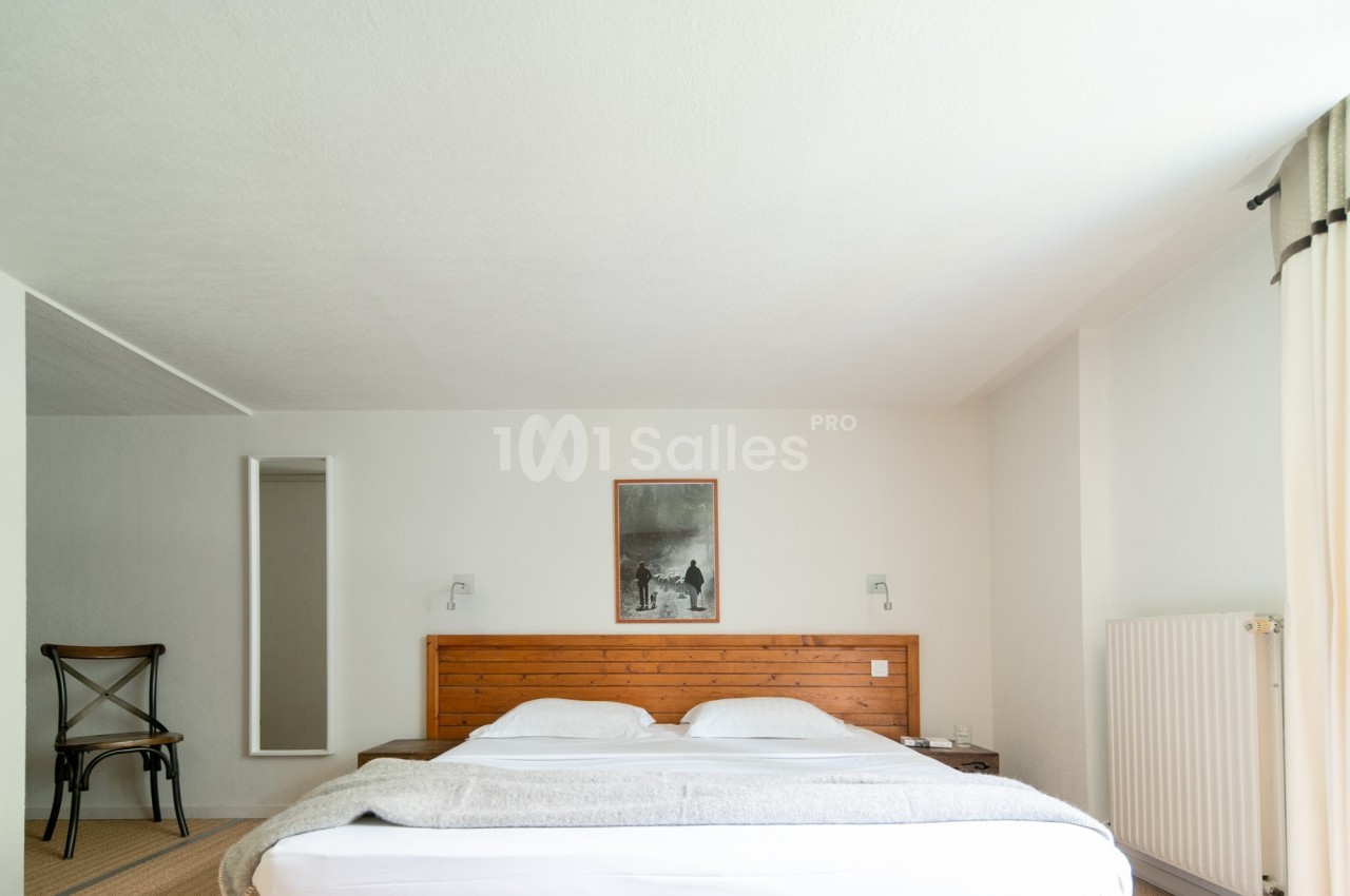 Chambre lumineuse avec un lit double, une tête de lit en bois, une chaise et un tableau au mur.