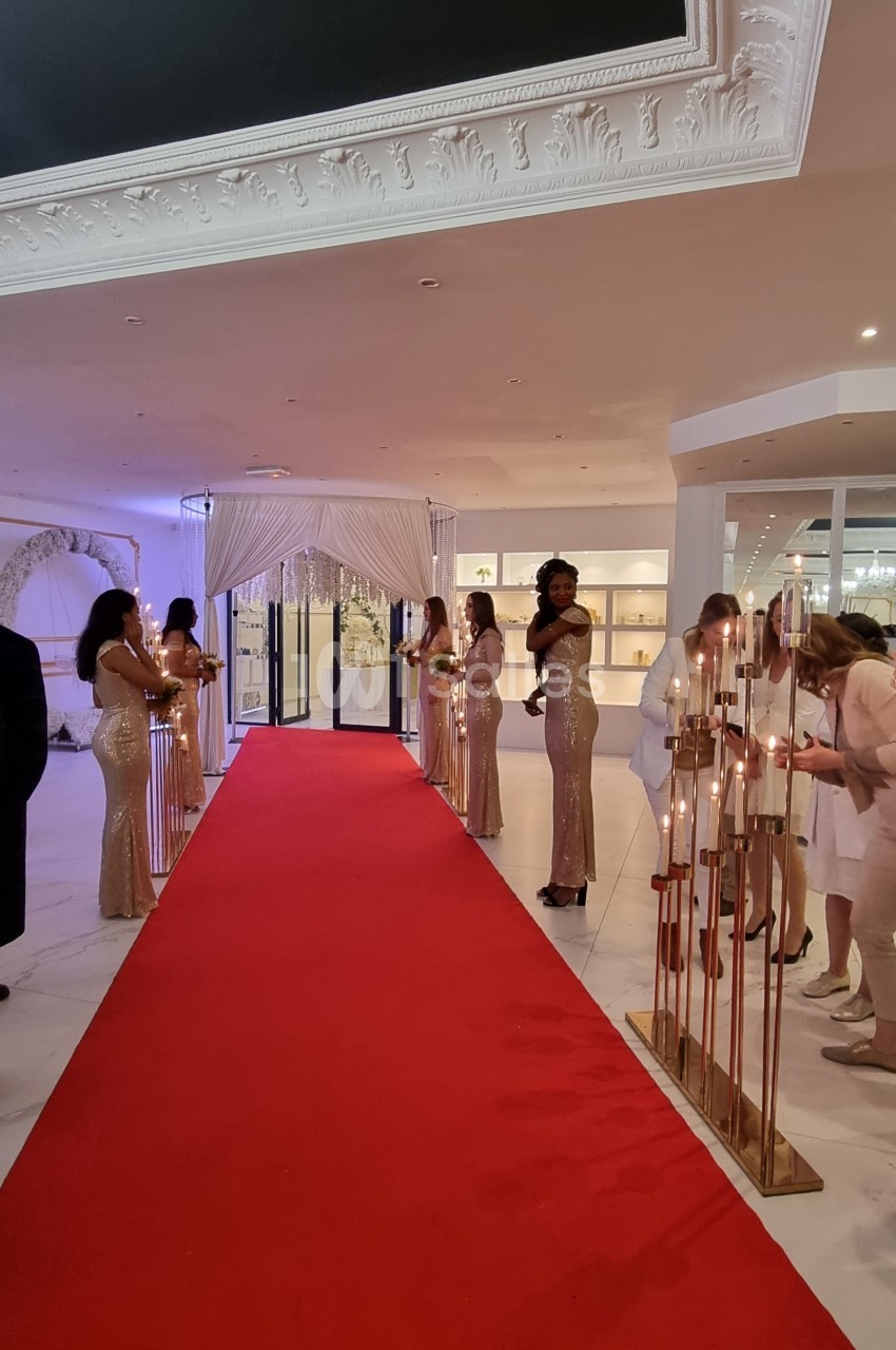Des hôtesses en robes dorées alignées le long d'un tapis rouge dans un espace intérieur élégant.