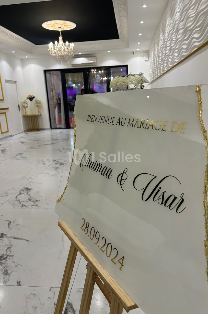 Panneau de bienvenue pour un mariage, placé dans une salle élégante avec décorations blanches et dorées.
