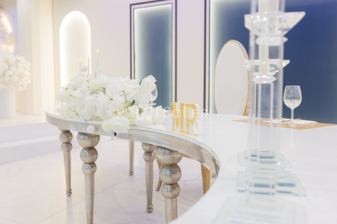 Table décorée avec des fleurs blanches, un panneau ’MR’ doré et des chandeliers dans un cadre élégant et lumineux.