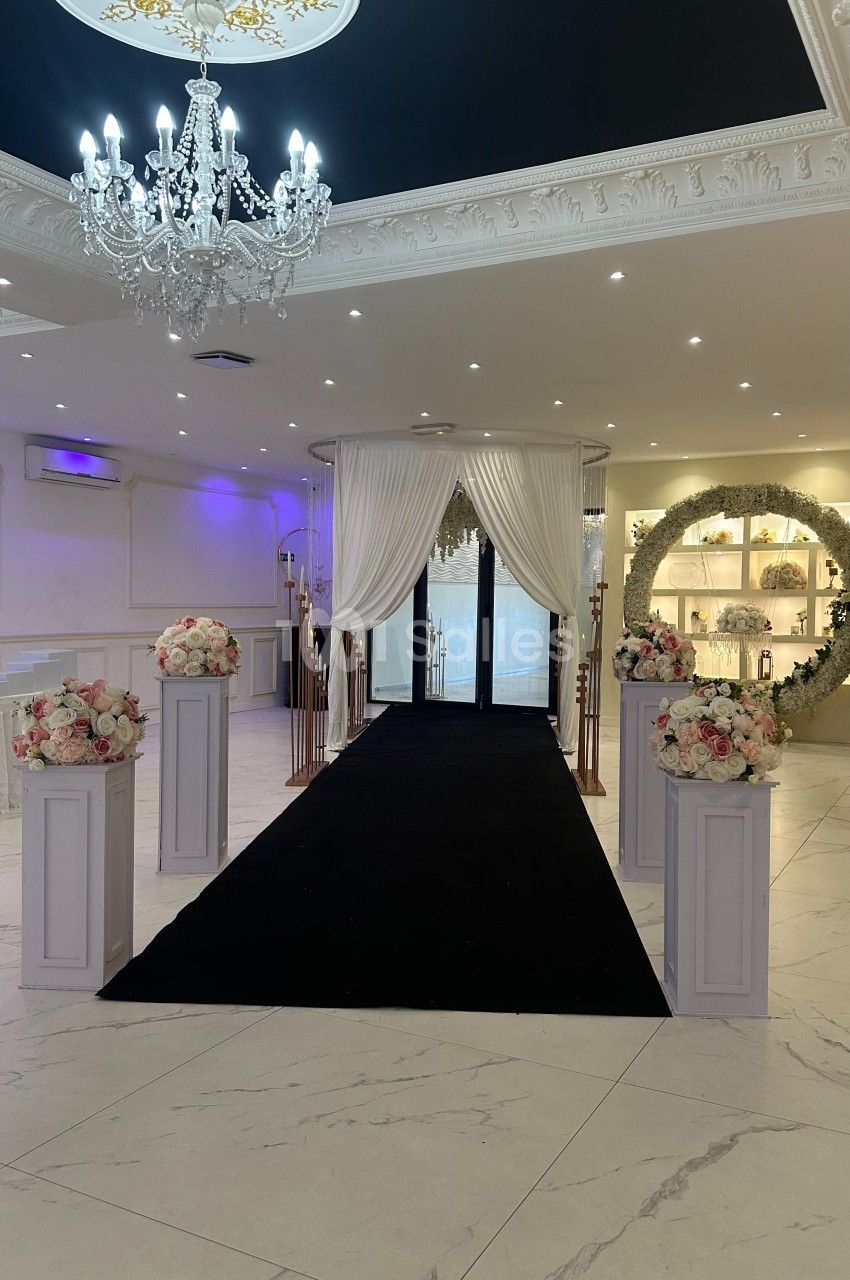 Allée décorée avec tapis noir, colonnes fleuries, rideaux blancs et arche florale dans une salle élégante.