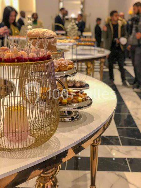 Table garnie de pâtisseries variées dans un cadre élégant avec des personnes en arrière-plan.
