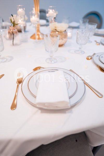 Table dressée avec vaisselle élégante, couverts dorés, serviette pliée et décoration florale blanche.
