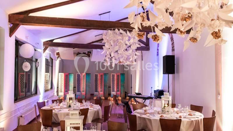 Salle de réception décorée avec des tables dressées, des luminaires suspendus et des cloisons colorées en arrière-plan.