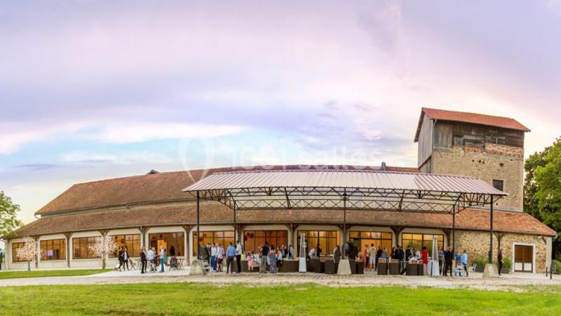 Bâtiment en pierre avec toit en tuiles, grande verrière et personnes rassemblées devant, sous un ciel dégagé.