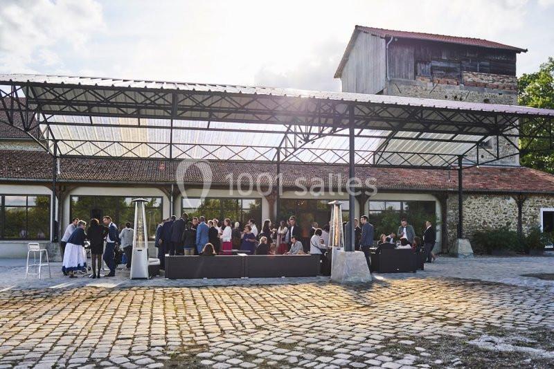 Groupe de personnes réunies en extérieur sous une structure métallique, devant un bâtiment en pierre et bois.