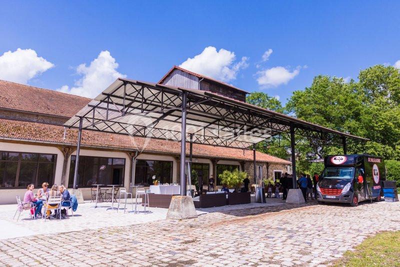 Un groupe de personnes assises à des tables en extérieur près d'un bâtiment avec une structure métallique et un food truck.