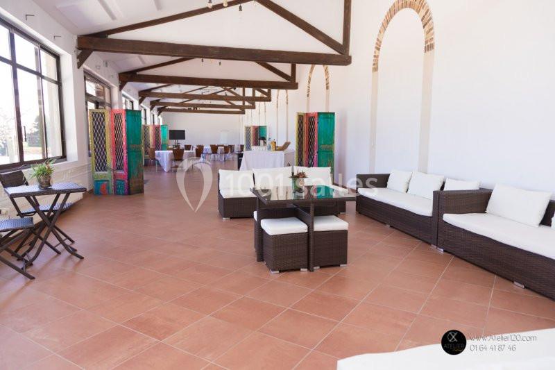 Salle lumineuse avec poutres apparentes, mobilier en rotin, tables dressées et paravents colorés en arrière-plan.