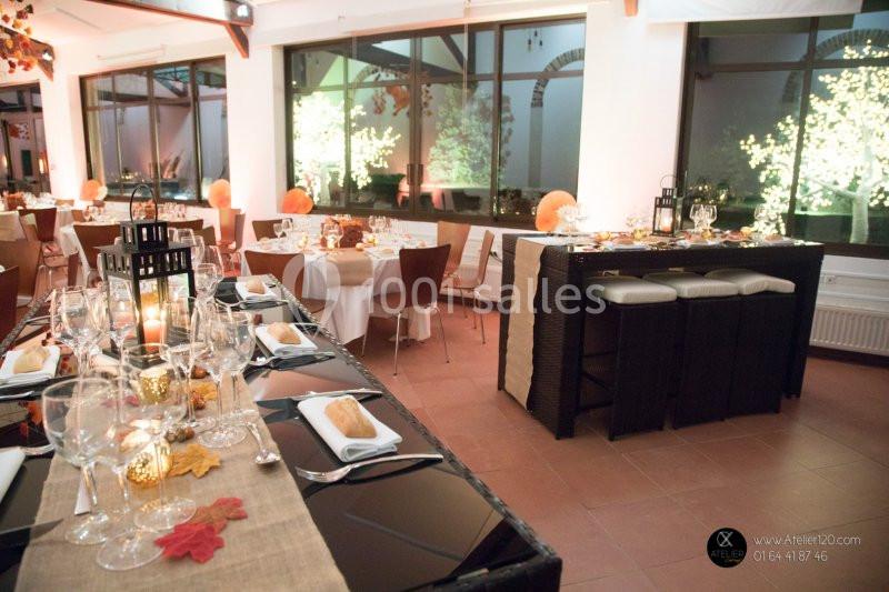 Salle de réception décorée pour un dîner, avec tables dressées, lanternes, feuilles d'automne et éclairage chaleureux.