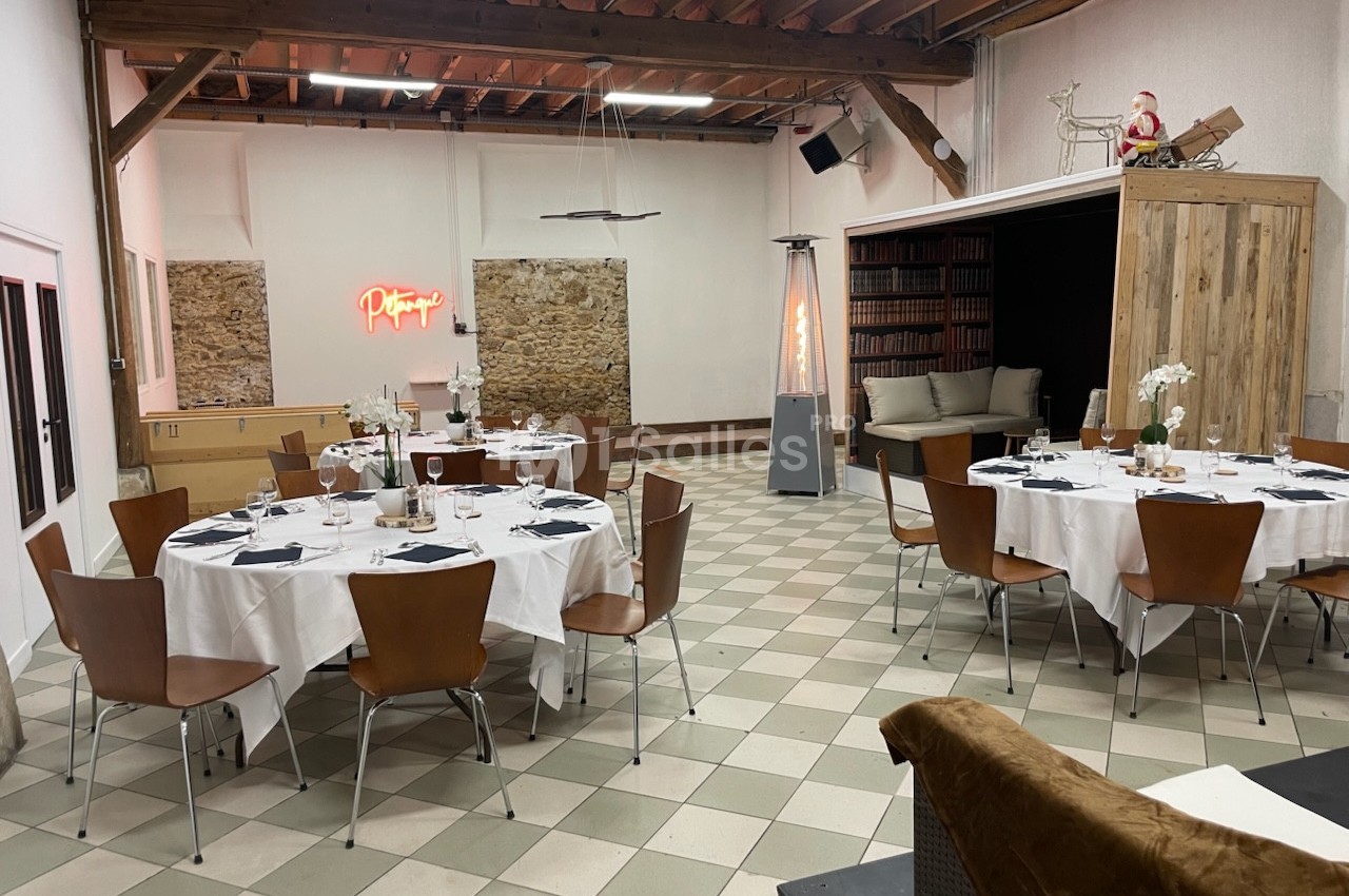 Salle de réception avec tables rondes dressées, chaises en bois, murs en pierre et décoration moderne.
