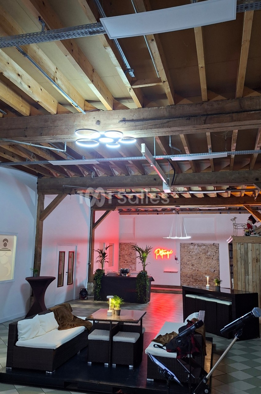 Espace intérieur avec poutres apparentes, mobilier lounge, éclairage tamisé et décoration végétale.