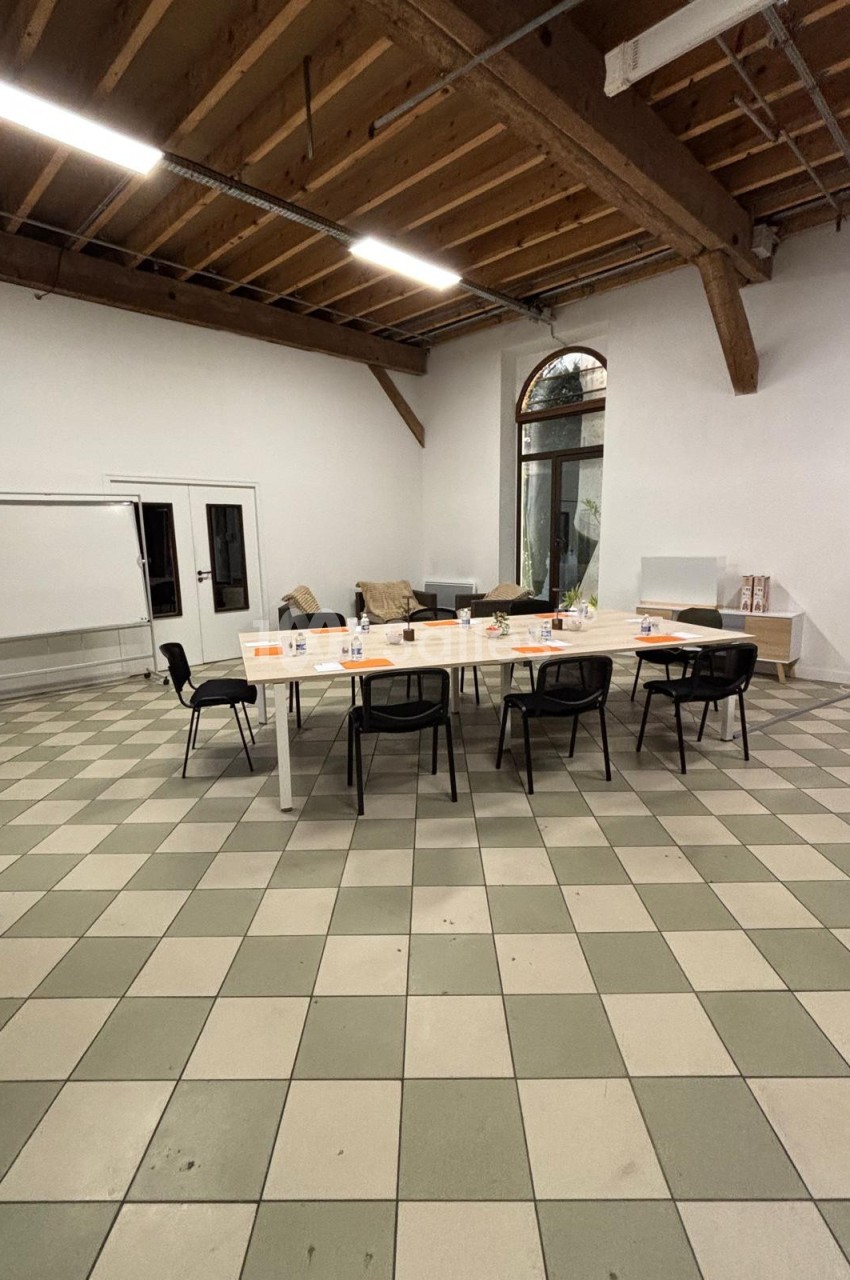Salle de réunion avec une grande table blanche entourée de chaises noires, tableau blanc et canapé en arrière-plan.