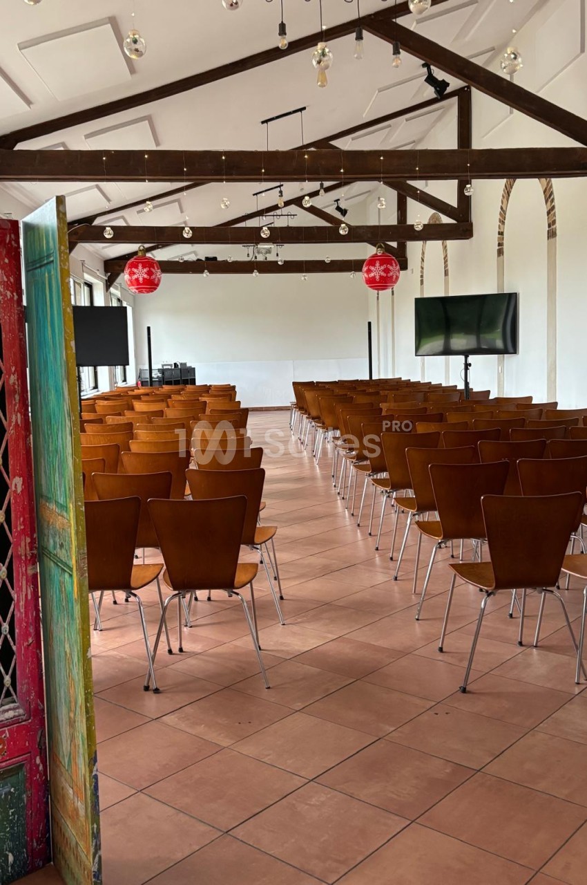Salle de conférence lumineuse avec rangées de chaises en bois, écrans et décorations suspendues.