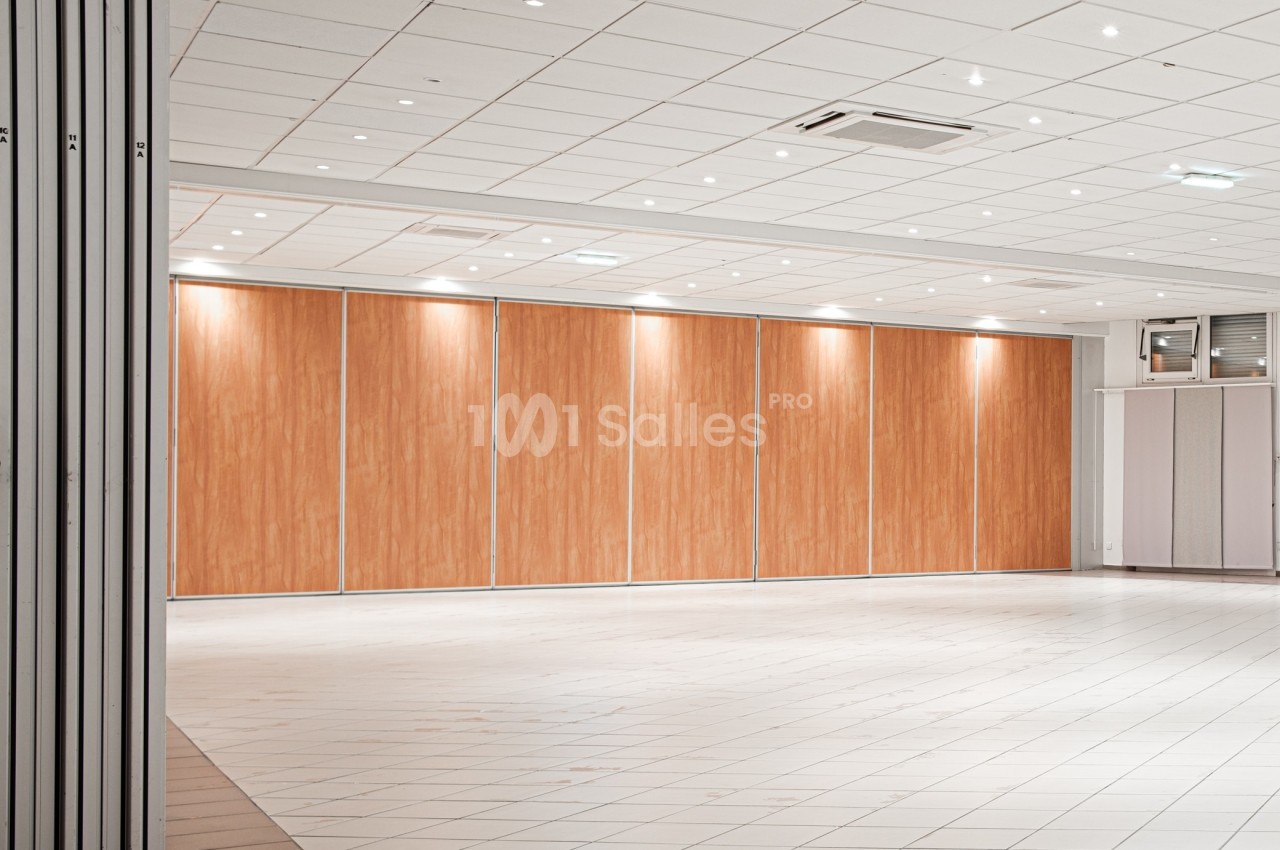Salle vide avec cloison amovible en bois clair, sol carrelé blanc et plafond équipé de spots lumineux.