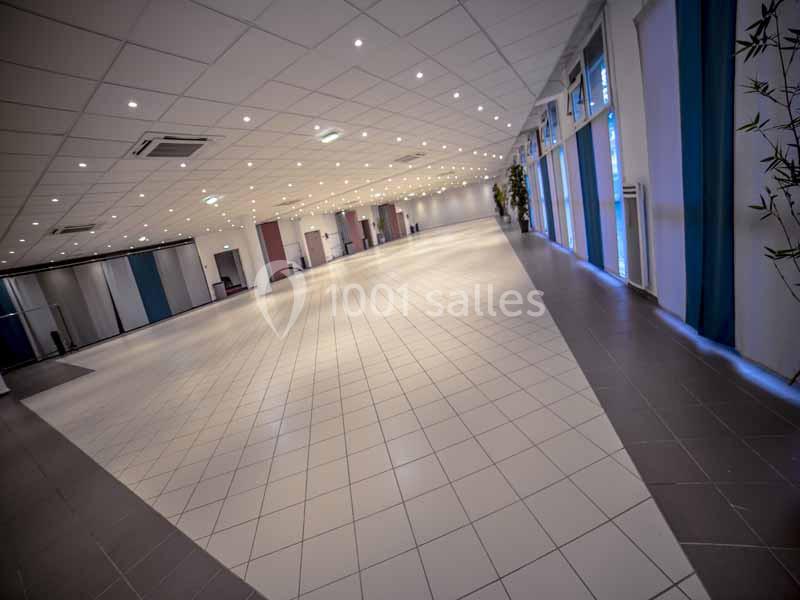 Salle spacieuse avec carrelage clair, plafond à dalles et éclairage intégré, entourée de grandes baies vitrées.