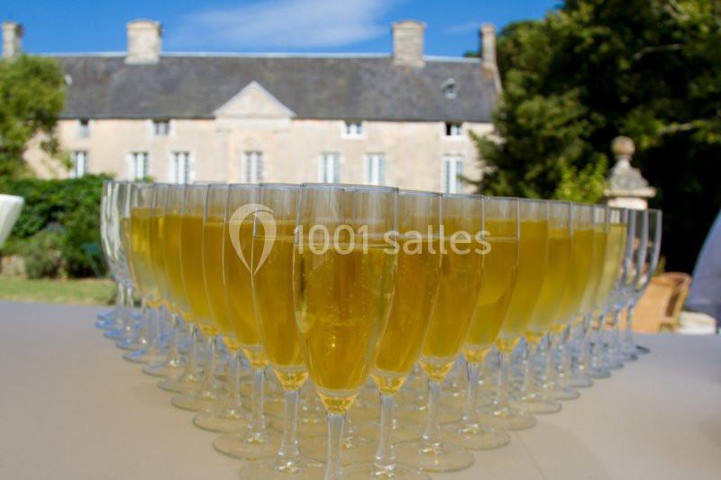 Verres de champagne alignés sur une table en extérieur, avec un bâtiment en pierre et des arbres en arrière-plan.