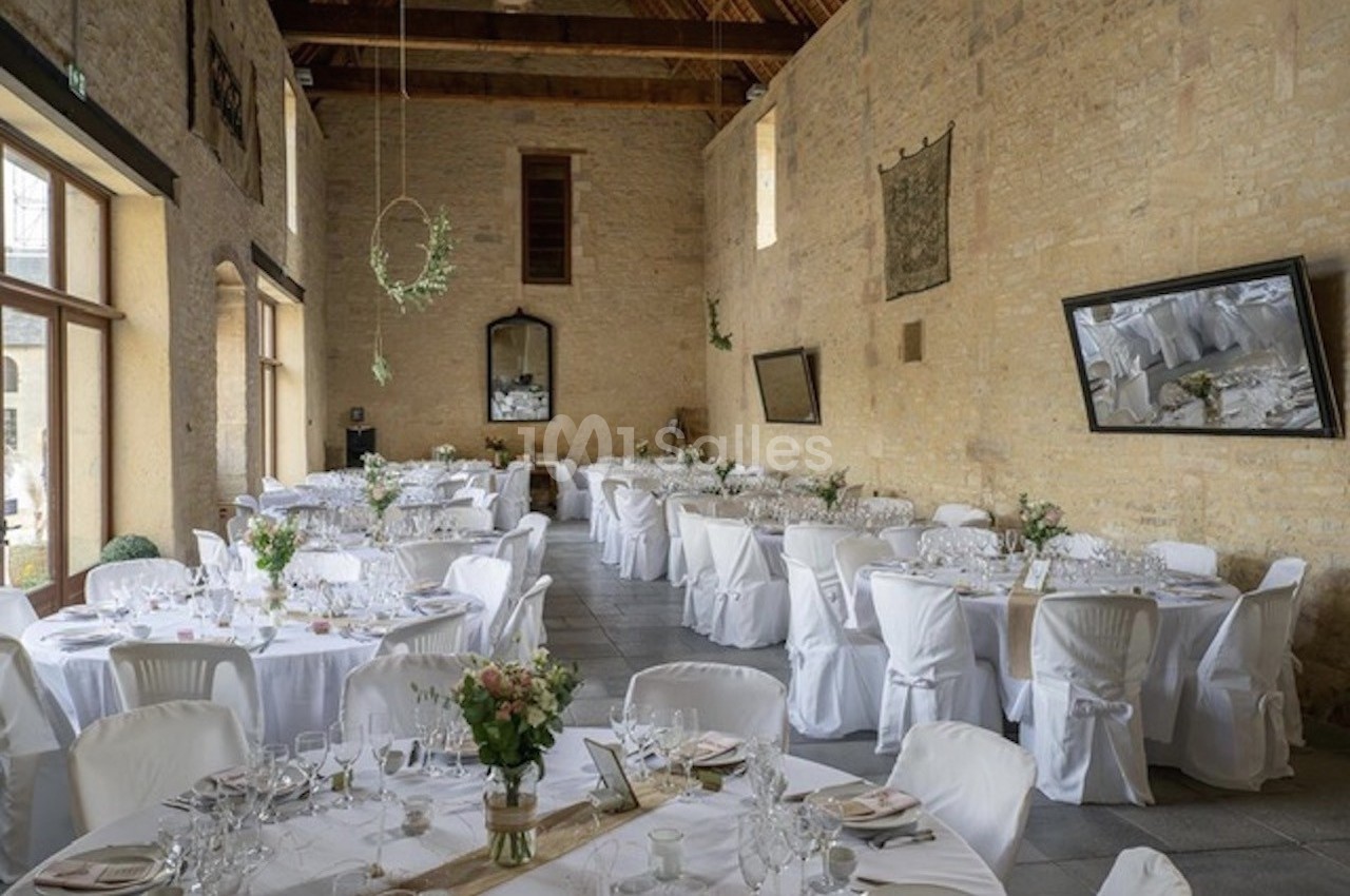 Salle de réception lumineuse avec tables rondes décorées de nappes blanches et compositions florales.