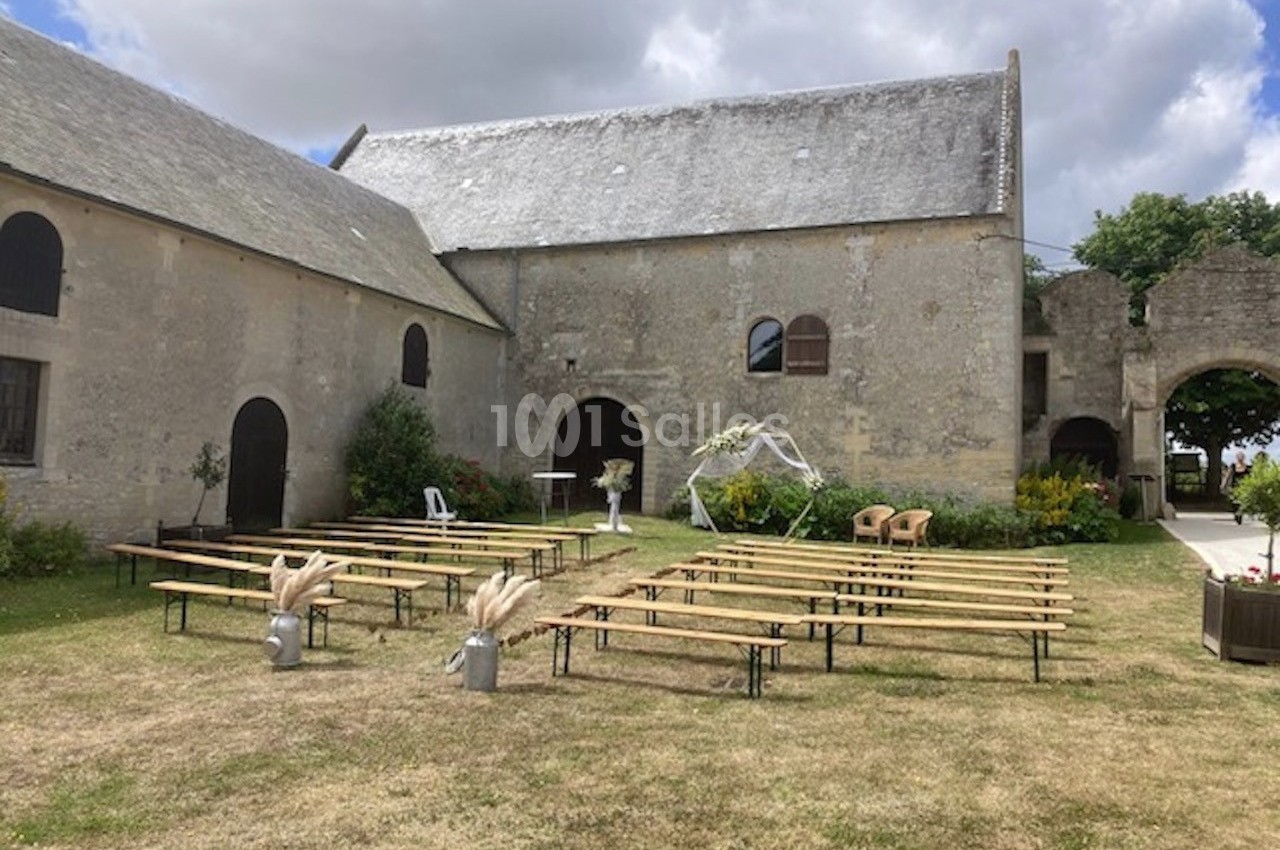 Bancs en bois disposés en extérieur devant un bâtiment en pierre, avec arche décorative et ciel partiellement nuageux.